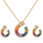 Gold necklace and matching earrings with curved horseshoe-shaped pendants featuring a rainbow of colored stones and clear pavé accents, shown on a white background.
