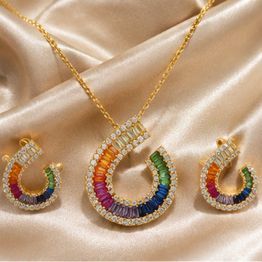 Gold crescent-shaped necklace and matching earrings set with rainbow-colored stones and clear crystal accents, displayed on a beige satin fabric background.
