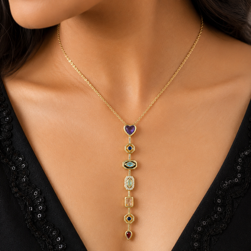 A gold-toned necklace with a vertical drop pendant featuring multiple colorful gemstone or enamel sections, worn on a model's neck over a black sequined top.