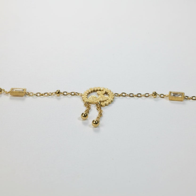 SVORA gold plated stainless steel bracelet with three heart charm, baguette CZs, and dangling beads. Adjustable.
