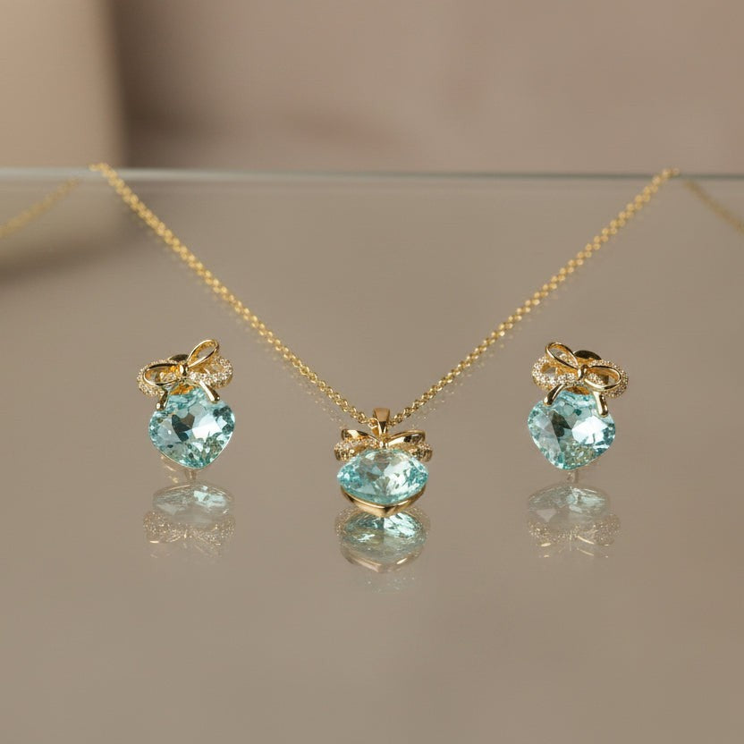 SVORA gold tone necklace and earrings set with aqua cushion-cut crystals and pavé bow details.