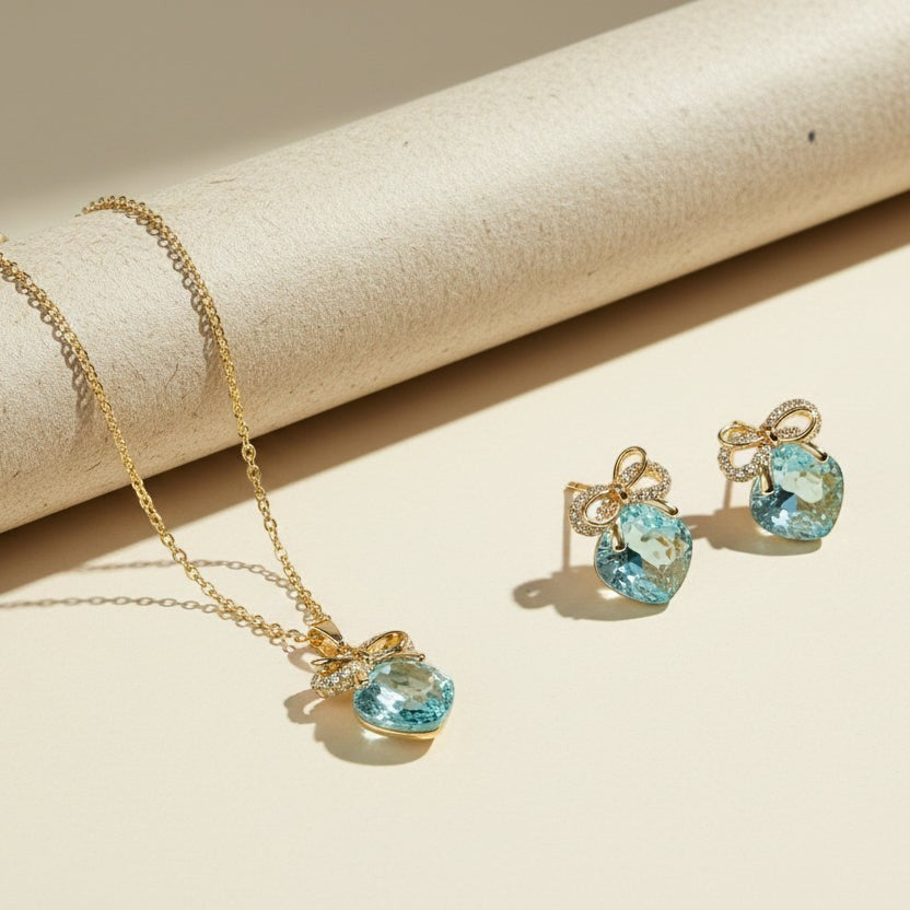 SVORA gold-tone necklace and earrings set with aqua cushion-cut crystals and pavé bow details.