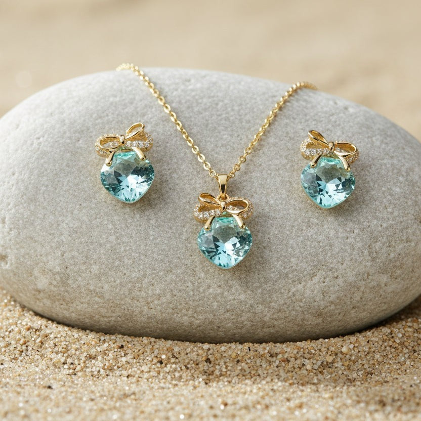 SVORA gold-tone necklace and earrings set with aqua cushion-cut crystals and pavé bow details.