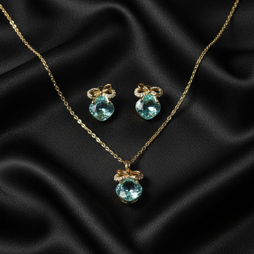 SVORA gold-tone necklace and earrings set with aqua cushion-cut crystals and pavé bow details.