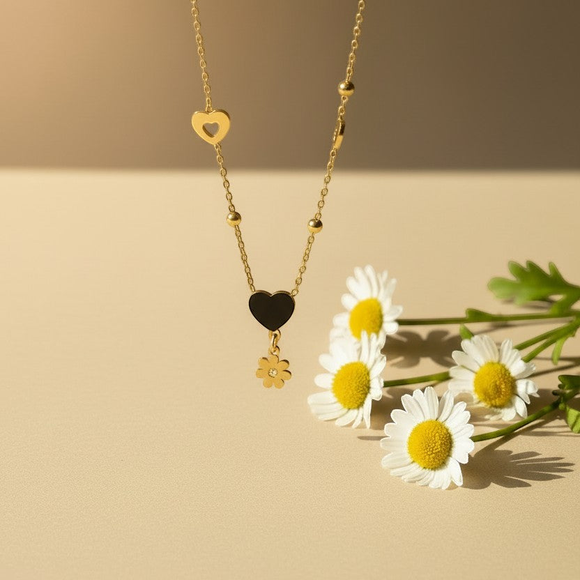 SVORA gold necklace with black enamel heart and daisy charm, gold beads, and hollow hearts.