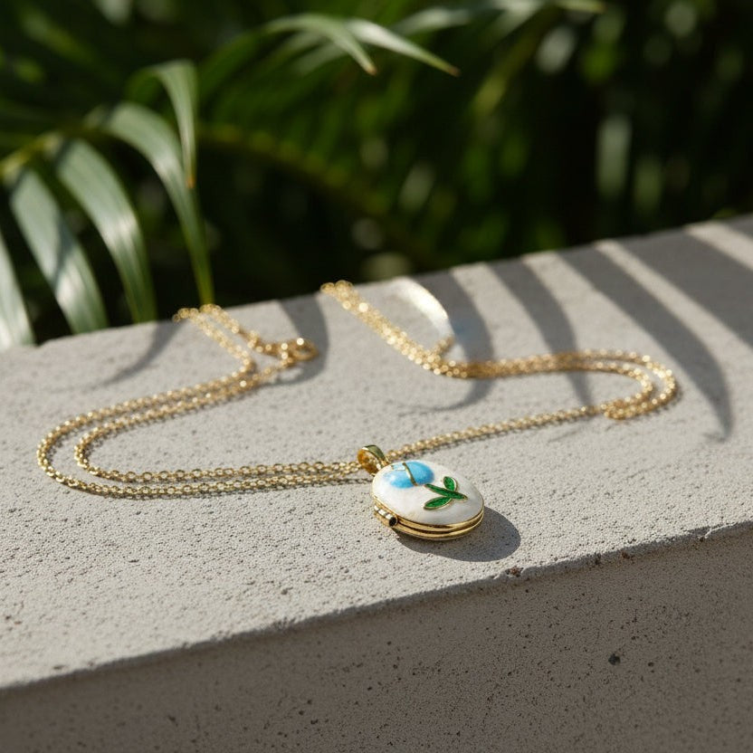 SVORA gold plated stainless steel locket necklace with a blue rose and green leaf enamel design on a mother-of-pearl disc.
