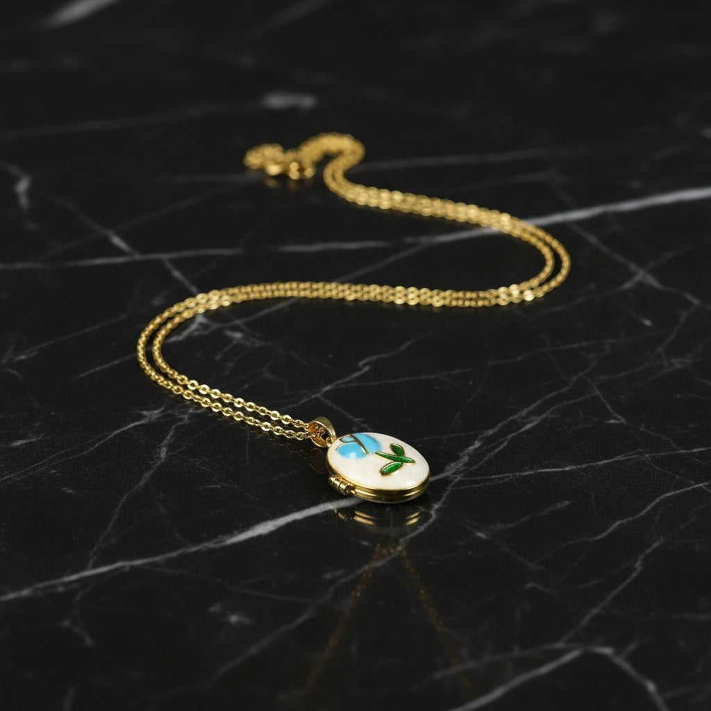 SVORA gold plated stainless steel oval locket necklace with blue rose and green leaf enamel detail.
