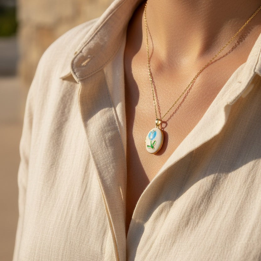 SVORA gold plated stainless steel pendant necklace with mother-of-pearl disc, blue enamel rose and green leaf.