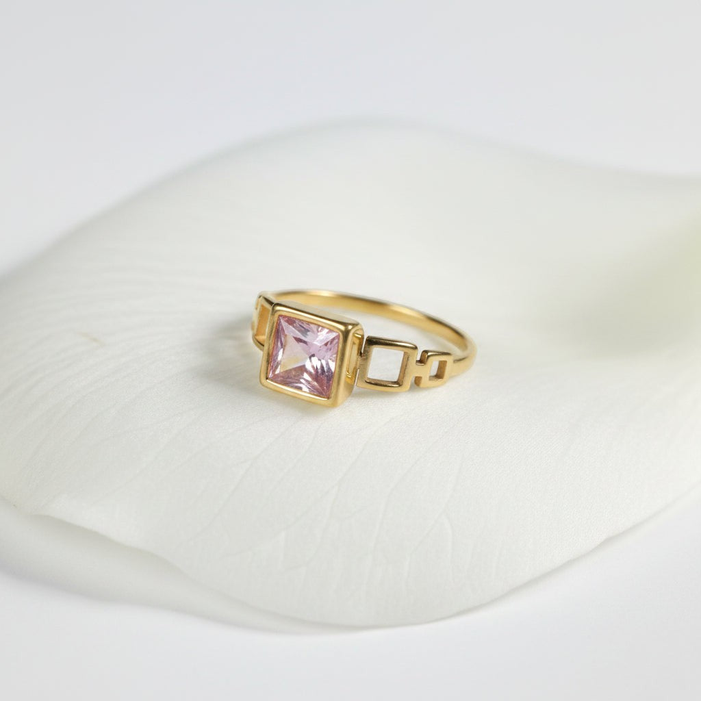 SVORA gold tone ring with a blush pink square-cut center stone and open square link details.