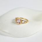 SVORA gold tone ring with a blush pink square-cut center stone and open square link details.
