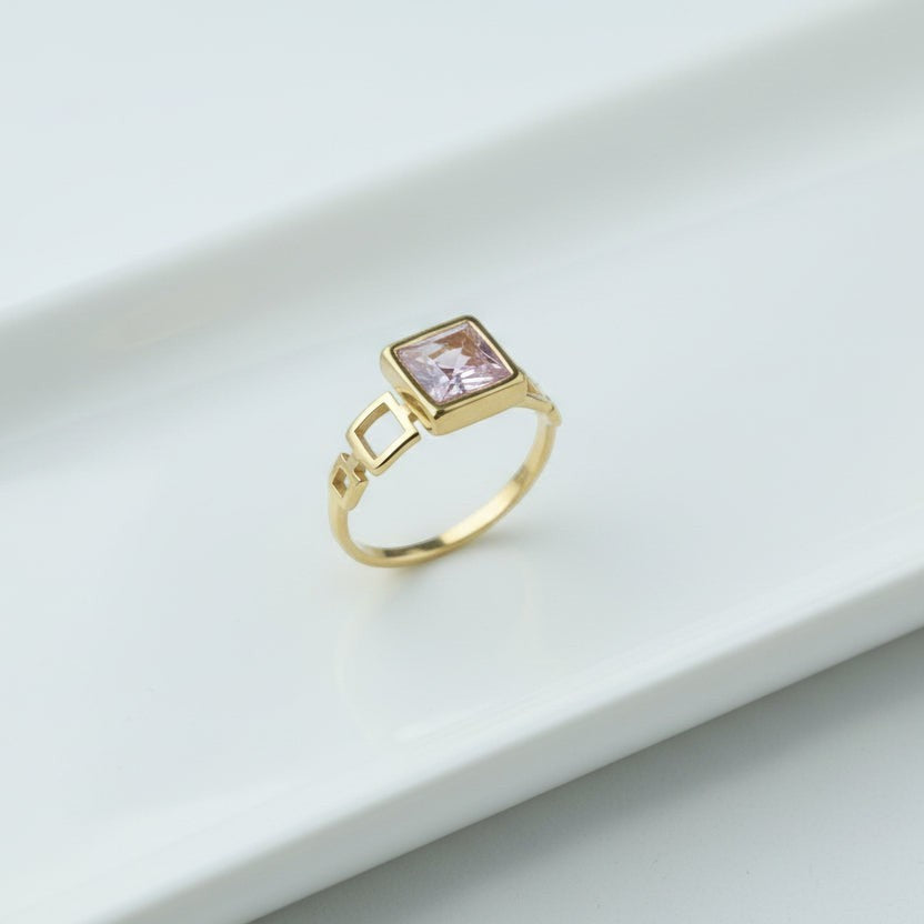 SVORA gold tone ring with a blush pink square-cut stone and geometric open links. 18K gold plated.