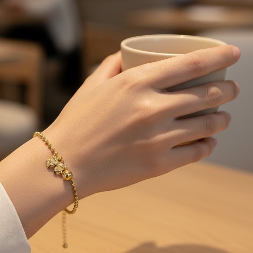 SVORA gold bow charm bead chain bracelet with a single gold ball charm. Adjustable, lobster clasp.