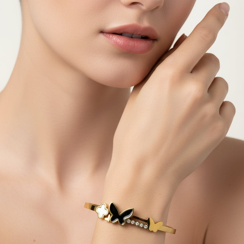 SVORA gold-plated stainless steel bracelet with black onyx butterfly, white pearl clover, and small gold butterfly.