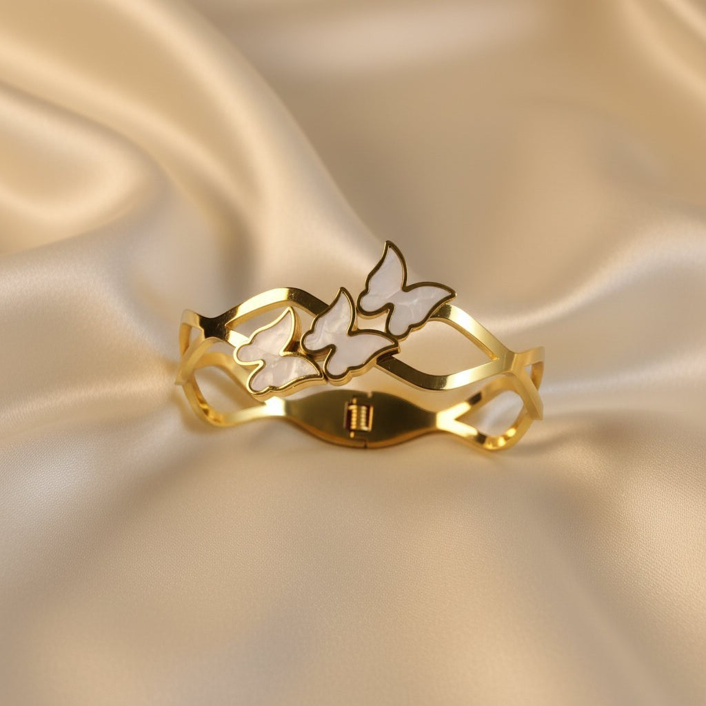 SVORA gold-plated stainless steel bracelet with three mother-of-pearl butterflies and wave-edged band.