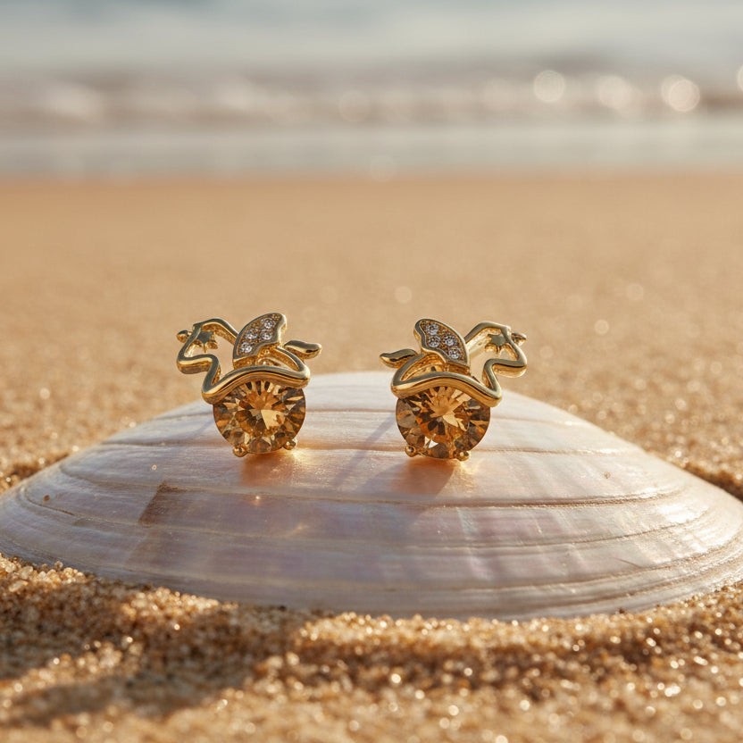 SVORA gold apple stud earrings with champagne crystals and small diamond accents, set on a seashell on a beach.