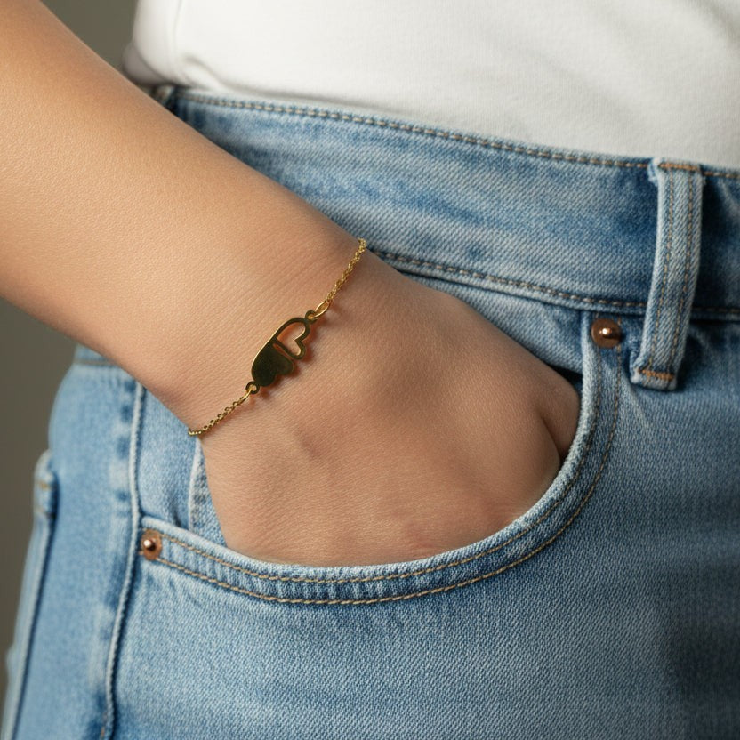 SVORA gold plated stainless steel bracelet with two connected hearts, one solid and one open, on a fine chain.
