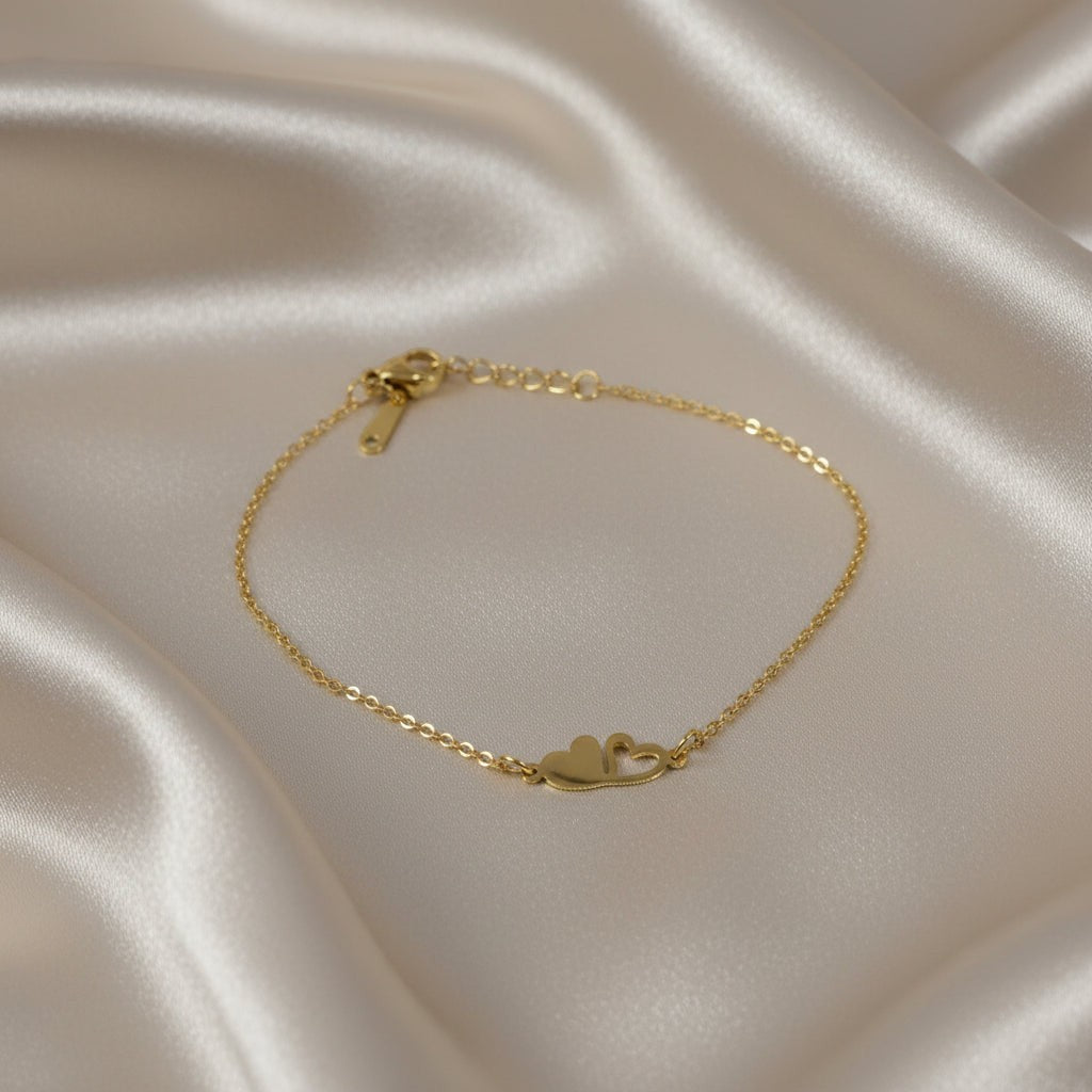 SVORA gold plated stainless steel bracelet with two connected hearts, one solid and one open. Adjustable.