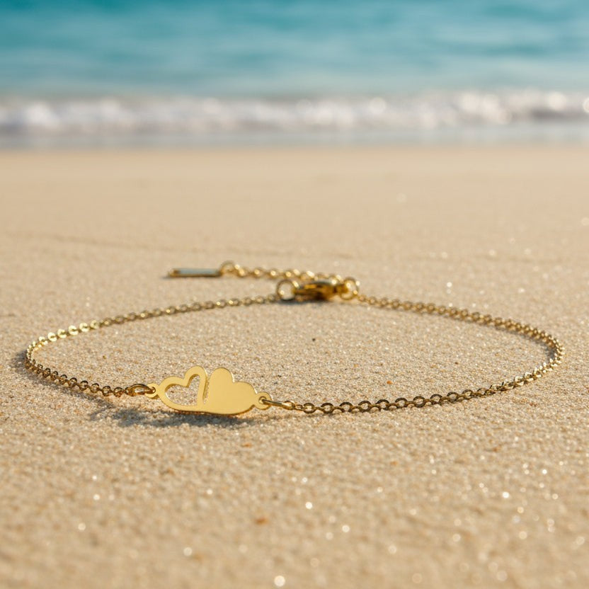 SVORA gold plated stainless steel bracelet with two connected hearts, one solid and one open, on a fine chain.