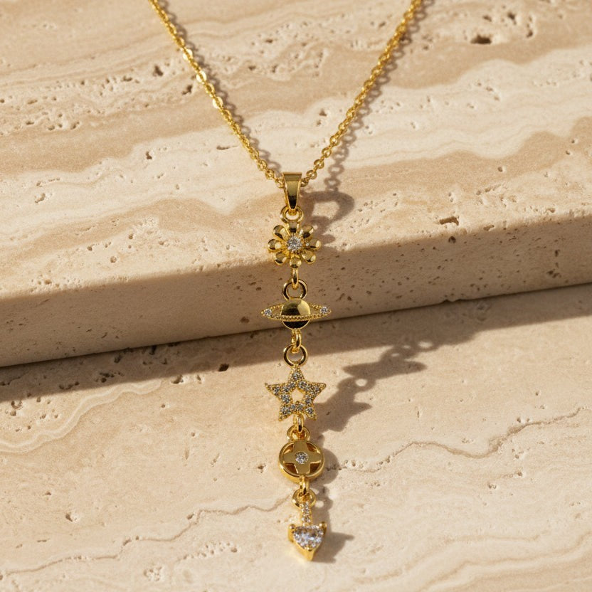 SVORA gold cable chain lariat necklace with dangling charms: daisy, Saturn, star, quatrefoil, and heart. 18K gold plated.