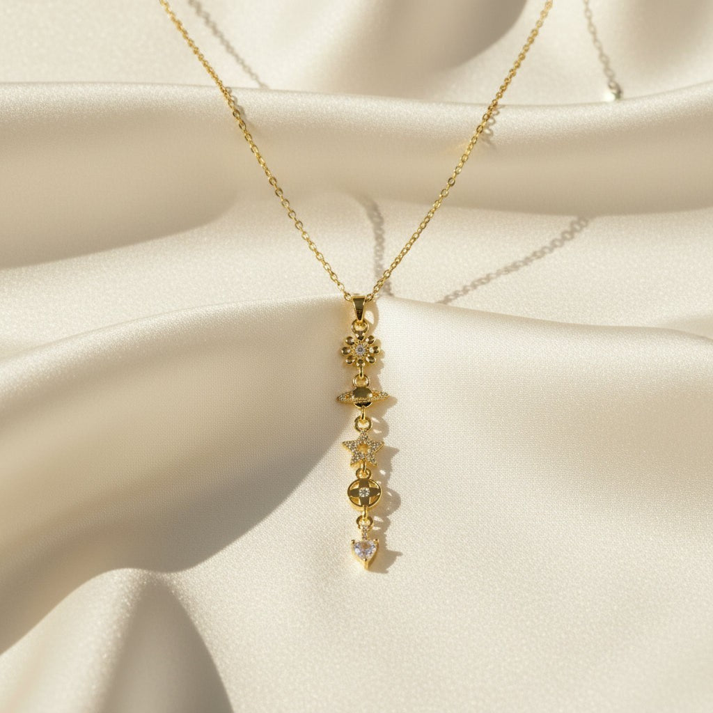 SVORA gold cable chain necklace with a vertical drop of charms including a daisy, Saturn, star, quatrefoil, and heart.