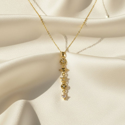 SVORA gold cable chain necklace with a vertical drop of charms including a daisy, Saturn, star, quatrefoil, and heart.