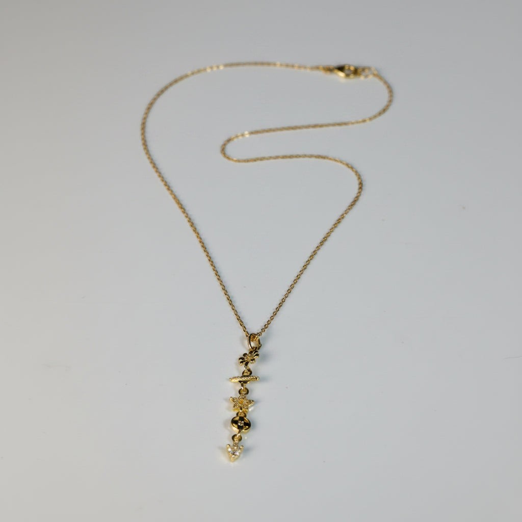 SVORA gold cable chain necklace with a vertical drop of charms including a daisy, Saturn ring, CZ star, quatrefoil, and heart.