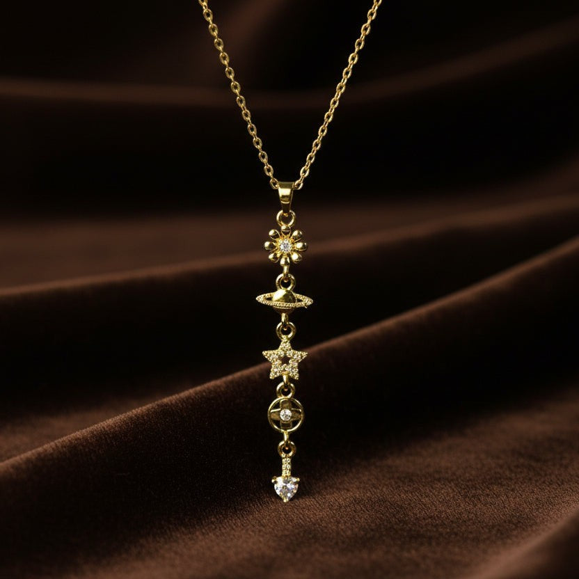 SVORA gold cable chain necklace with vertical drop of daisy, Saturn, star, circle, and heart charms.