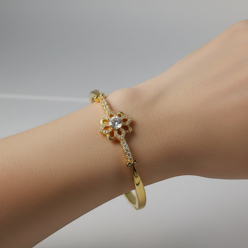 SVORA gold-plated stainless steel bracelet with a central flower design adorned with cubic zirconia stones and milgrain edging.