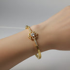 SVORA gold-plated stainless steel bracelet with a central flower design adorned with cubic zirconia stones and milgrain edging.