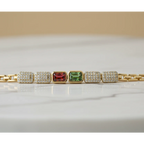 SVORA gold-tone adjustable bracelet with alternating rectangular red and green gemstones and diamond-encrusted links.