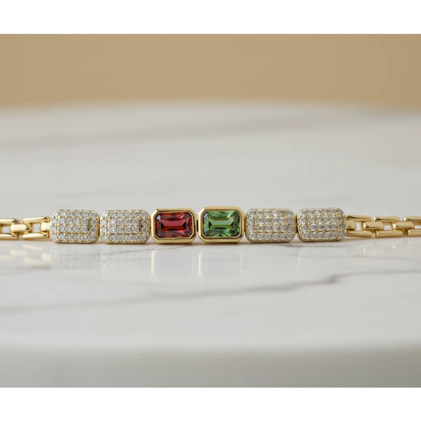 SVORA gold-tone adjustable bracelet with alternating rectangular red and green gemstones and diamond-encrusted links.