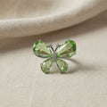 SVORA Ethereal Emerald Butterfly Ring with pear-cut green wings and pavé body on a textured background.