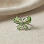 SVORA Ethereal Emerald Butterfly Ring with pear-cut green wings and pavé body on a textured background.