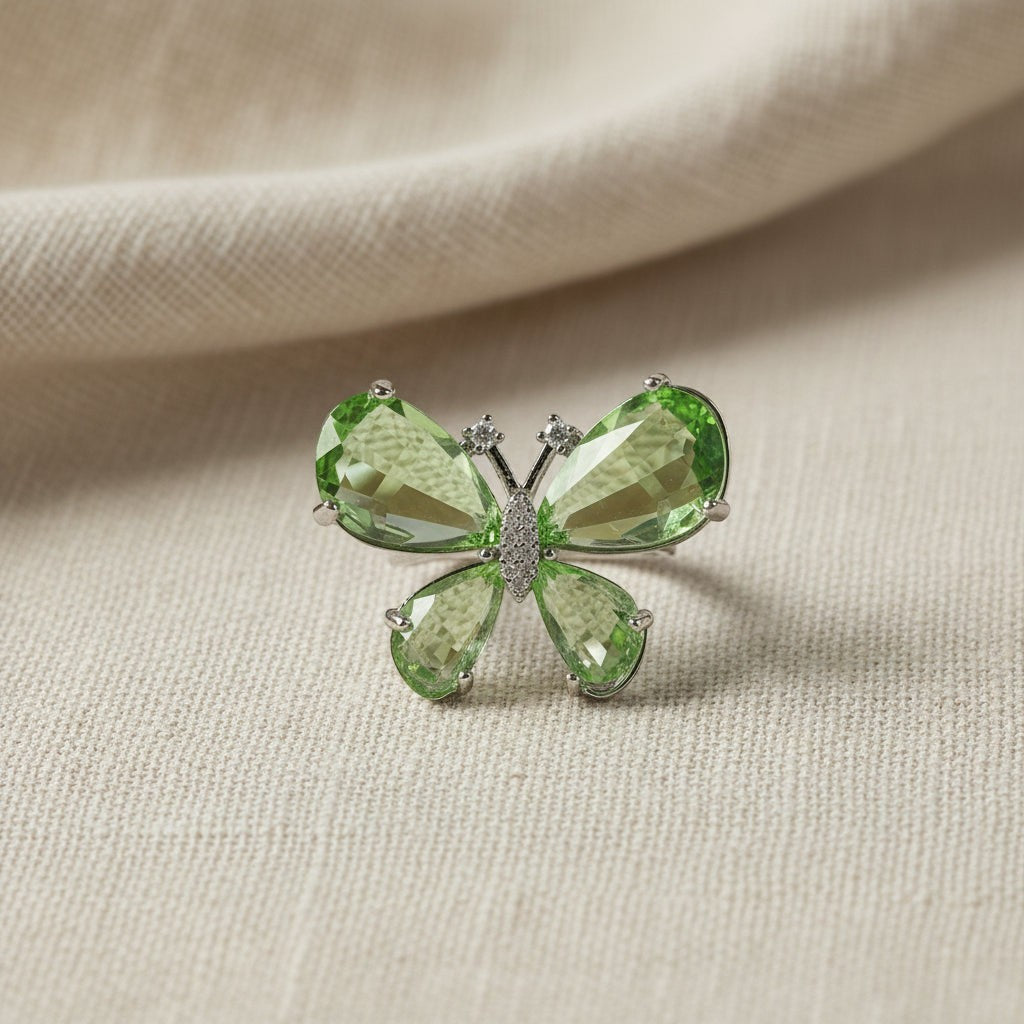 SVORA Ethereal Emerald Butterfly Ring with pear-cut green wings and pavé body on a textured background.