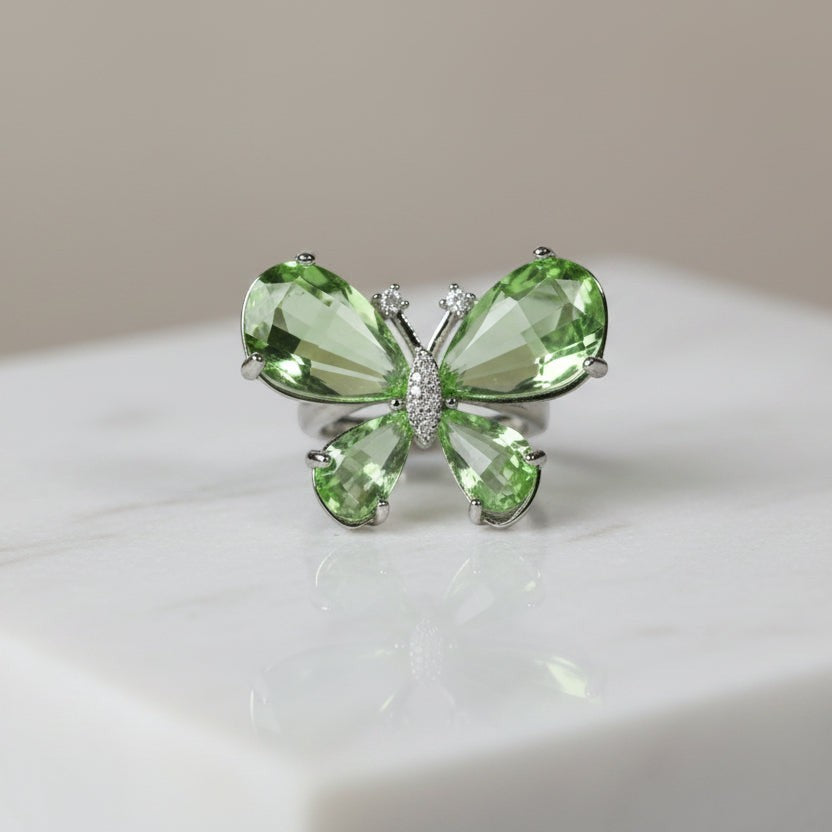 SVORA Ethereal Emerald Butterfly Ring with pear-cut green wings and pavé body on a marble surface.