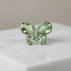 SVORA Ethereal Emerald Butterfly Ring with pear-cut green wings and pavé body on a marble surface.