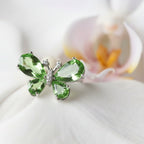 SVORA Ethereal Emerald Butterfly Ring with pear-cut green wings and pavé body on a white orchid.
