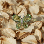 SVORA Ethereal Emerald Butterfly Ring with pear-cut green wings and pavé body on a bed of dried petals.