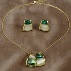SVORA gold-tone necklace and earrings set with emerald green and cream cabochon stones in a caged design.