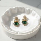 SVORA gold-tone drop earrings with pavé heart studs, bow connectors, and emerald crystal heart drops.