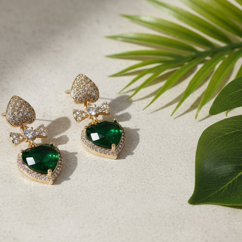 SVORA gold-tone earrings with pavé heart studs, bow connectors, and emerald crystal heart drops.