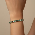 SVORA Emerald Tennis Adjustable Bracelet with green and clear baguette-cut stones on a gold-tone band.