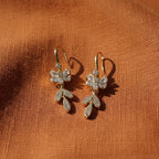 SVORA Flora Stones Dangler Earrings: Gold-tone stainless steel earrings with clear cubic zirconia in a floral design.