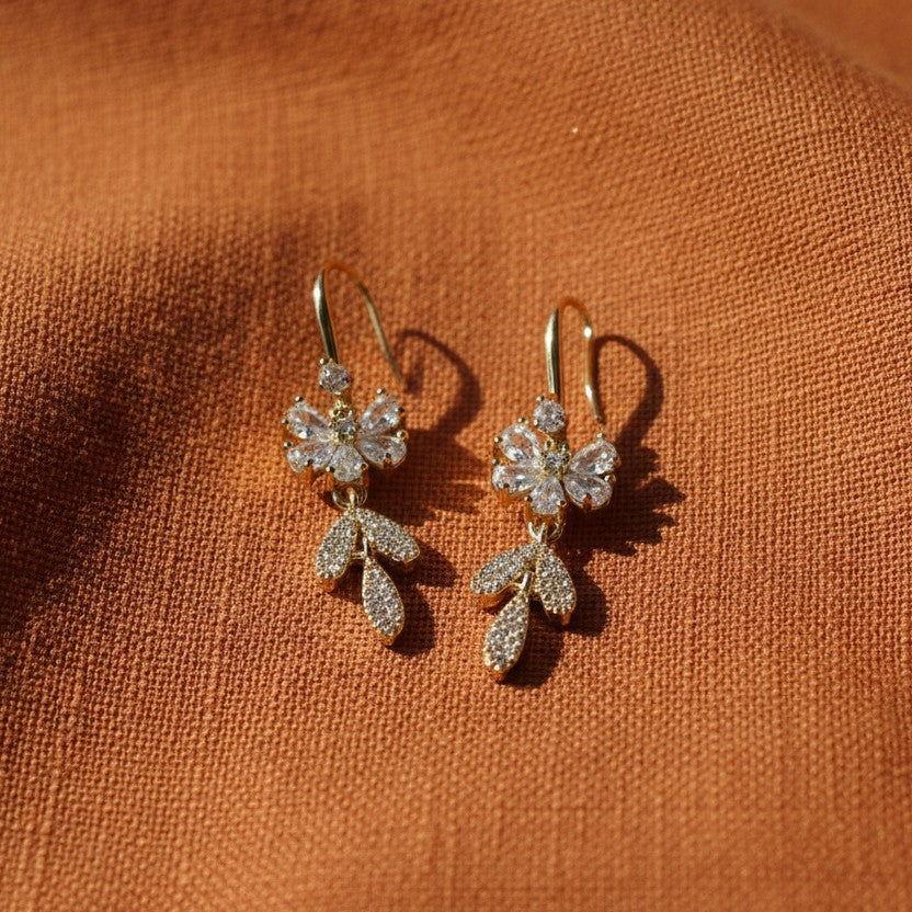 SVORA Flora Stones Dangler Earrings: Gold-tone stainless steel earrings with clear cubic zirconia in a floral design.