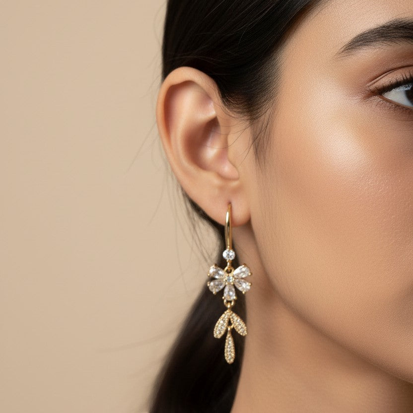 SVORA Flora Stones Dangler Earrings: Gold-tone stainless steel earrings with clear cubic zirconia in a floral design.