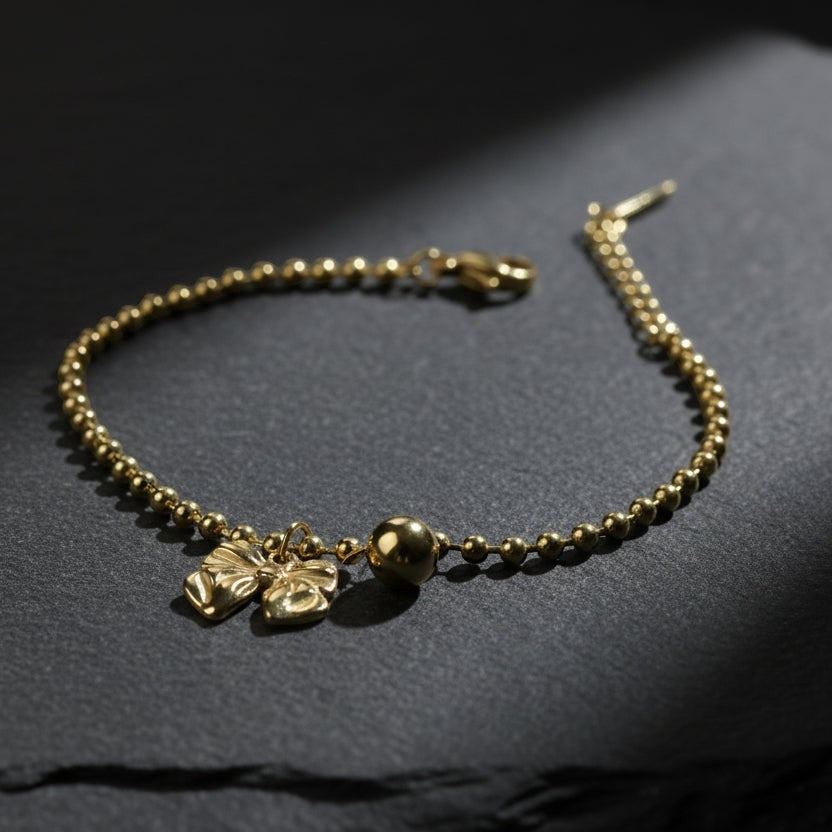 SVORA gold-plated stainless steel bracelet with bow and ball charms on a bead chain. Adjustable lobster clasp.