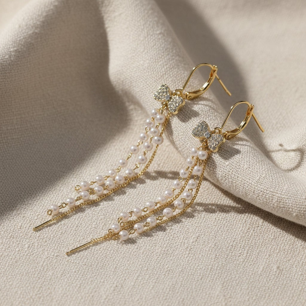SVORA gold-tone stainless steel dangle earrings with pavé bow, pearls, and cubic zirconia. Sui Dhaaga style.