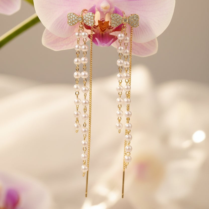 SVORA gold tone dangle earrings with pavé bow tops and cascading pearls and chains.