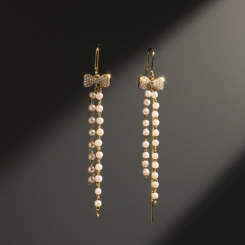 SVORA gold tone dangle earrings with pavé bow top and cascading freshwater pearls and chains.