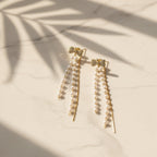 SVORA gold tone dangle earrings with pavé bow tops and cascading freshwater-style pearls and chains.